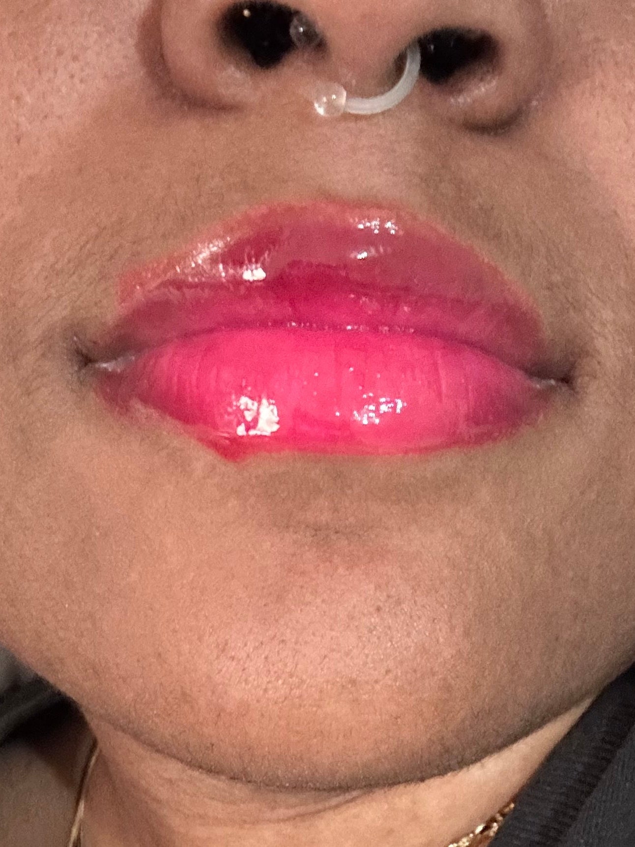 Close-up of a person wearing bright pink lipstick and a black garment with gold text.